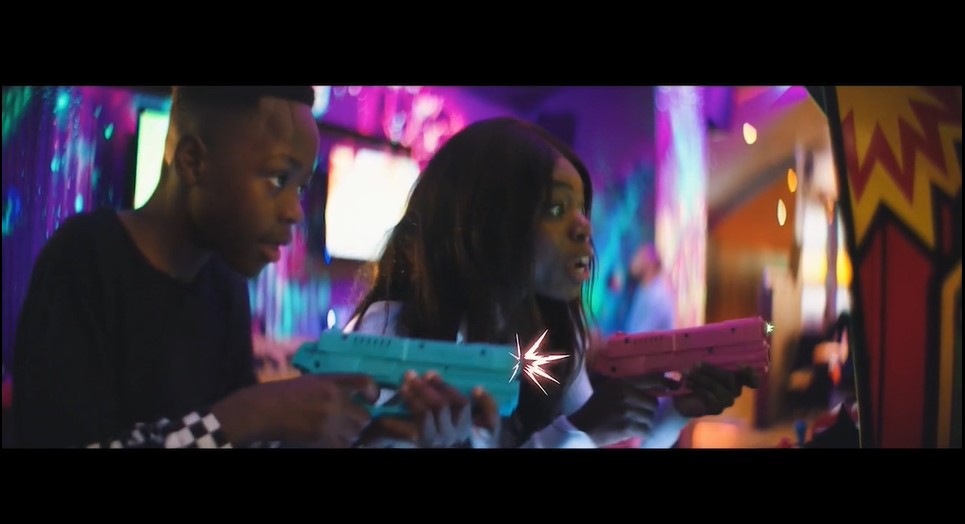 Two young black actors playing an arcade game with plastic guns